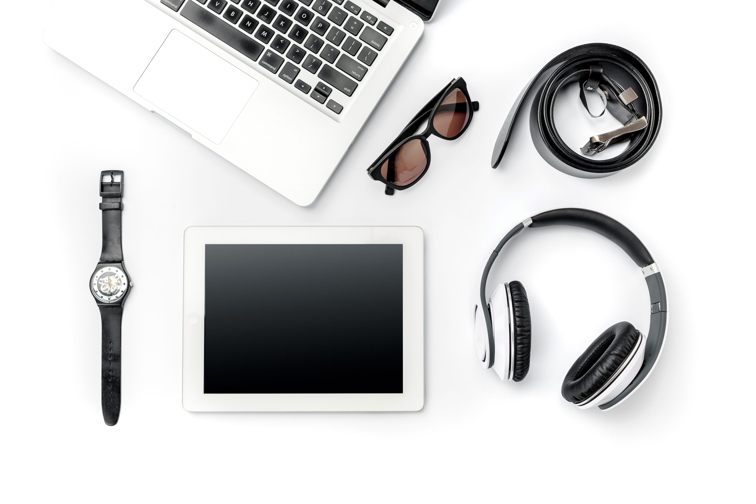 Notebook, tablet, fones de ouvido, relógio de pulso e óculos escuros sobre uma mesa
